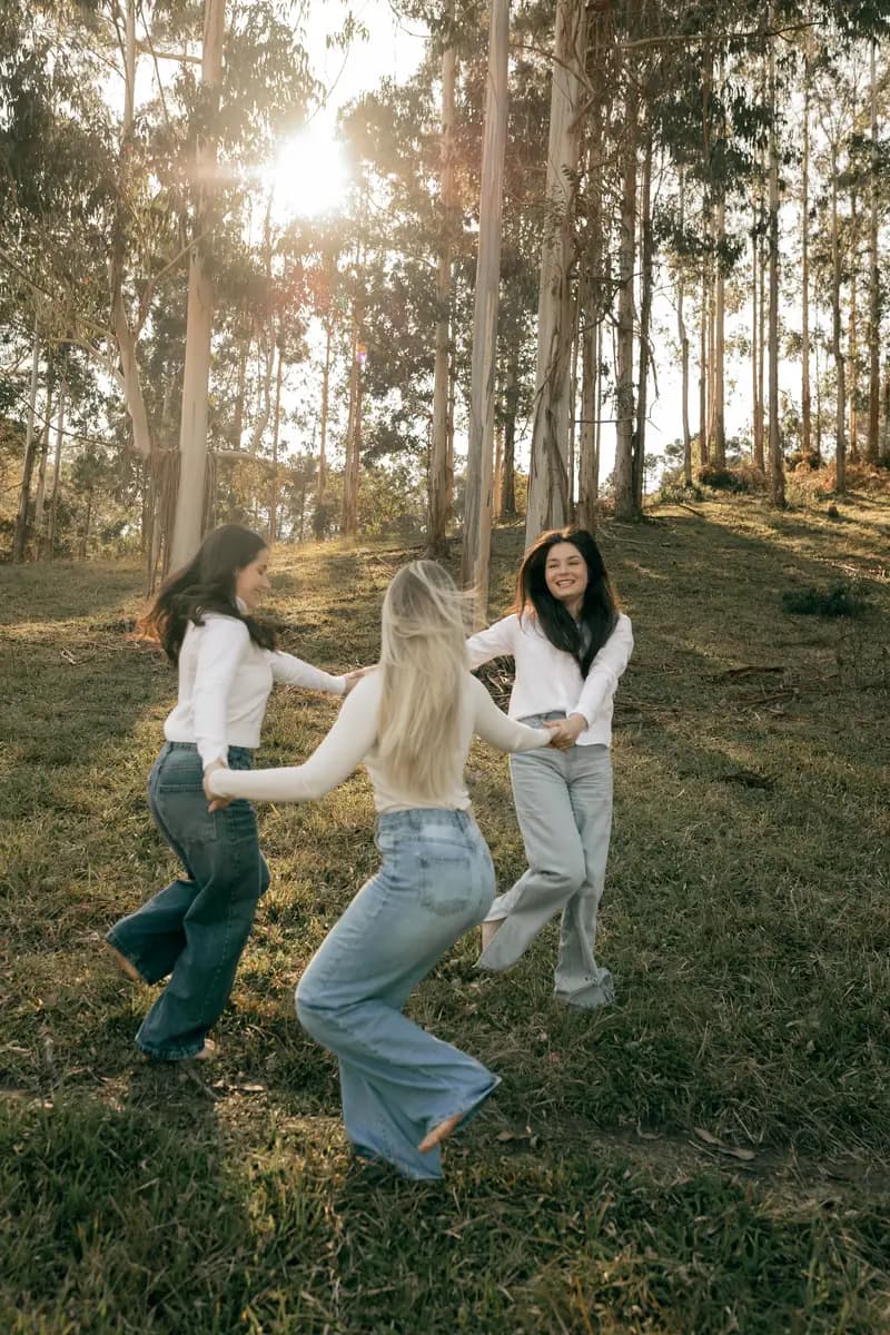 Three friends dancing together in a sunlit forest clearing